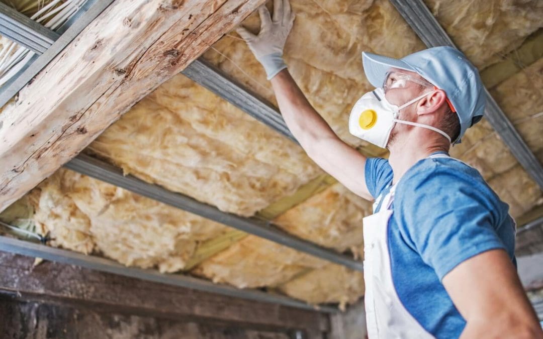A man in a blue shirt with a mask is checking attic insulation. The right insulation will help you heat your home efficiently.